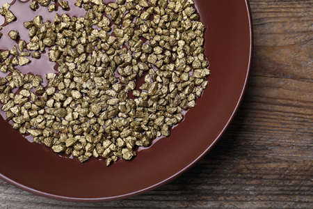 Plate of gold nuggets on wooden table, top view