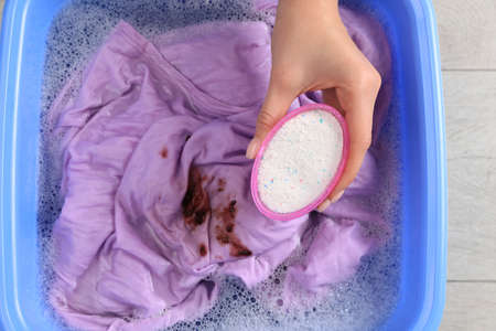 Woman adding powdered detergent into basin with clothes, top view. hand washing laundry