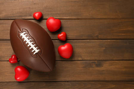 American football ball and hearts on wooden background, flat lay. Space for textの写真素材