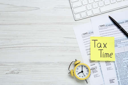 Reminder note with words Tax Time, documents, computer keyboard and alarm clock on white wooden table, flat lay. Space for textの写真素材