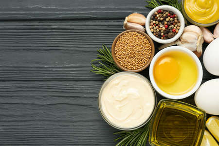 Glass bowl with fresh mayonnaise and ingredients on black wooden table, flat lay. Space for text