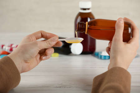 Woman pouring cough syrup into spoon at white wooden table, closeupの写真素材