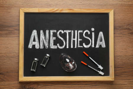 Blackboard with word Anesthesia, vials, mask and syringes on wooden table, top viewの写真素材