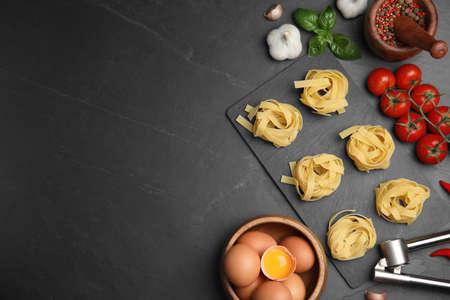 Flat lay composition with uncooked tagliatelle and fresh ingredients on black table. Space for textの写真素材