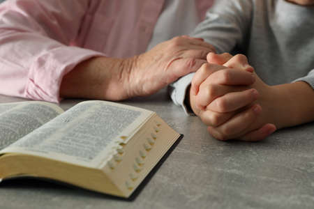 Boy and his godparent praying together at gray table, closeup