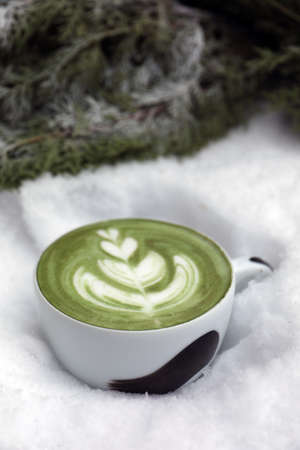 Cup of fresh matcha latte in snow outdoors