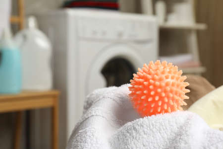 Orange dryer ball and towels near washing machine in laundry room, closeup. Space for textの写真素材