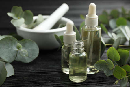 Bottles of eucalyptus essential oil and plant branches on black wooden table. Space for textの写真素材