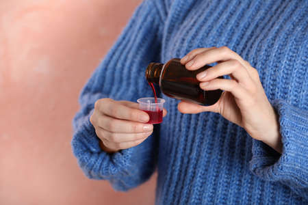 Woman pouring cough syrup into measuring cup on pink background, closeupの写真素材