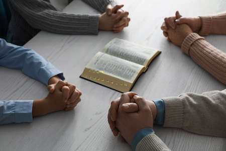 Boy and his godparents praying together at white wooden table, closeupの写真素材