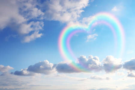 Beautiful view of heart shaped rainbow and white clouds in blue sky on sunny dayの写真素材