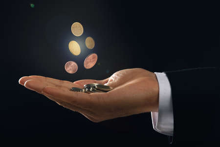Man and coins falling into his hand on black background, closeupの写真素材