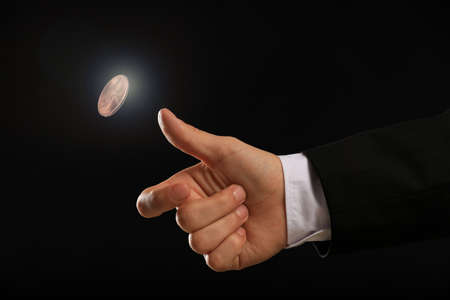 Man throwing coin on black background, closeup. making decisionの写真素材