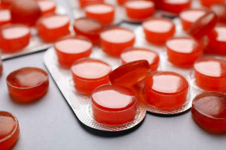 Orange cough drops on gray background, closeup