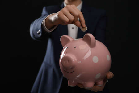 Woman putting coin into piggy bank on black background, closeupの写真素材