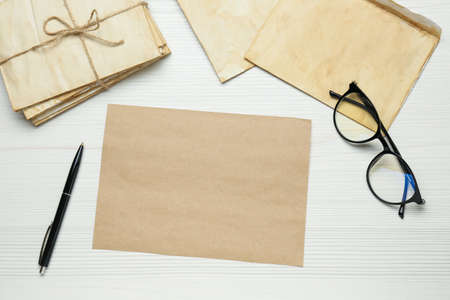 Old letters, blank card, pen and glasses on white wooden table, flat lay