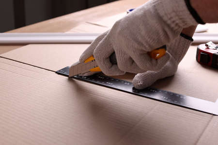 Worker cutting cardboard with utility knife and ruler, closeupの写真素材