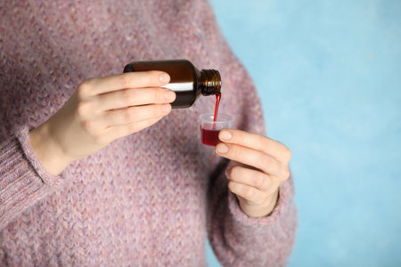 Woman pouring cough syrup into measuring cup on light blue background, closeupの写真素材