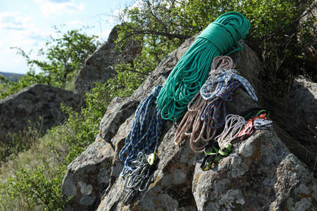 Different ropes and other climbing equipment on rocks outdoors, space for text
