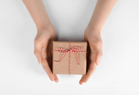 Woman holding parcel wrapped in kraft paper on white background, top view