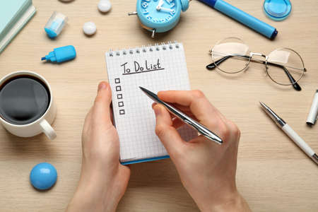 Woman filling To Do list in notepad at wooden table, top view