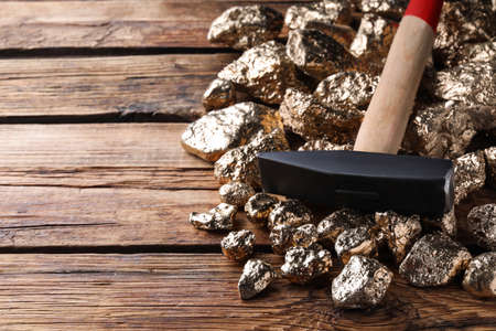 Pile of gold nuggets and hammer on wooden table, closeup. Space for textの写真素材