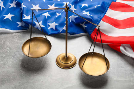 Scales of justice and American flag on light gray table