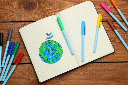 Happy Earth Day. Notebook with drawing of planet and markers on wooden table, flat layの写真素材
