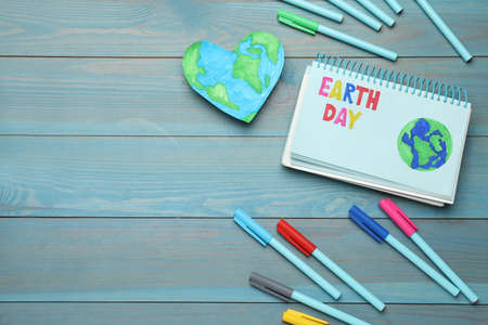 Happy Earth Day. Flat lay composition with notebook and markers on turquoise wooden table, space for...