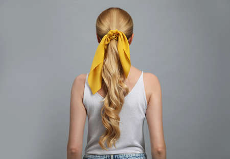 Young woman with stylish bandana on gray background, back view