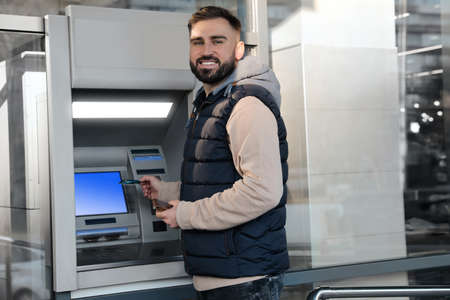Young man with credit card near cash machine outdoorsの写真素材