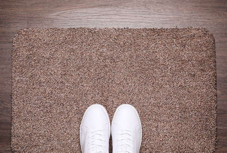 Stylish door mat and shoes on wooden floor, top view