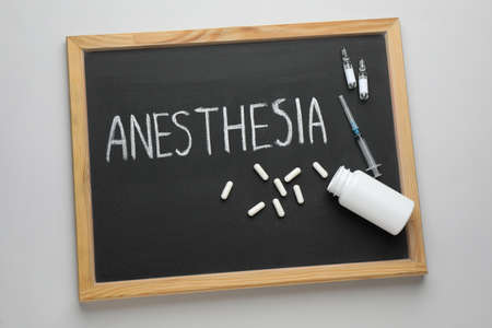 Blackboard with word Anesthesia, syringe and drugs on light gray background, top viewの写真素材