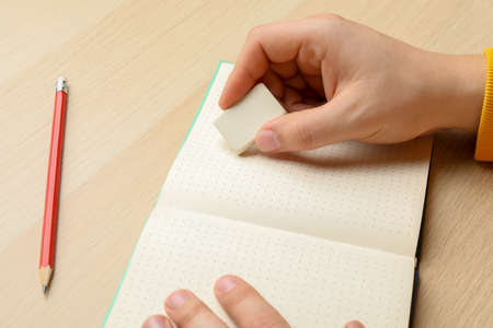 Man erasing something in notebook at wooden table, closeupの写真素材