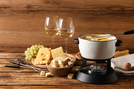 Pot of tasty cheese fondue, snacks and wine on wooden tableの写真素材