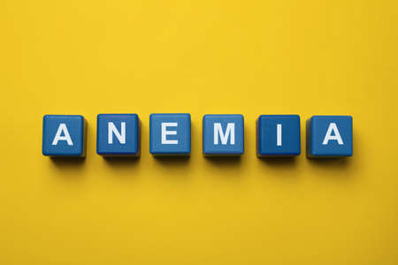 Word Anemia made with blue wooden cubes on yellow background, flat layの写真素材