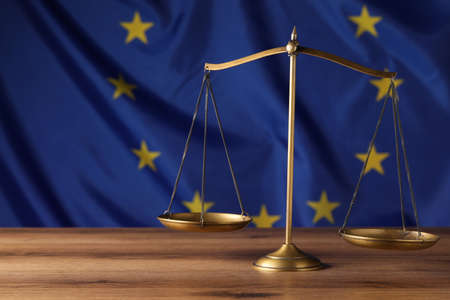 Scales of justice on wooden table against European Union flag. Space for textの写真素材