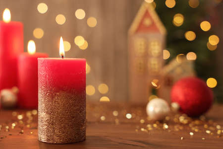 Beautiful burning candles with Christmas decor on wooden table against blurred festive lights, space for textの写真素材