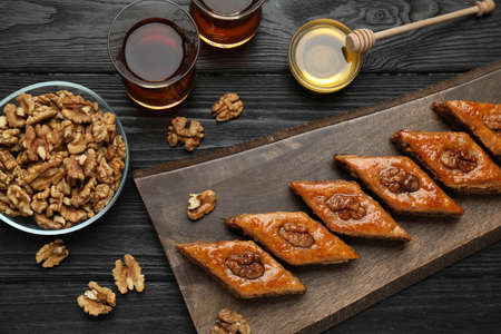 Delicious sweet baklava with walnuts, honey and hot tea on black wooden table, flat layの写真素材