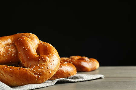 Tasty freshly baked pretzels on wooden table against black background. Space for textの写真素材