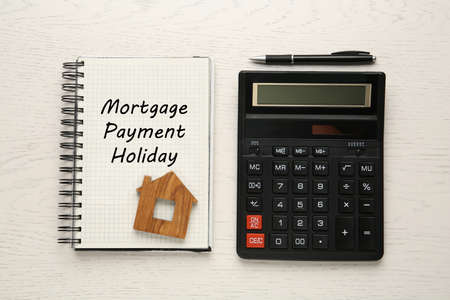 Notebook with words Mortgage Payment Holiday, house model, calculator and pen on white wooden table, flat layの写真素材