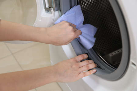 Woman cleaning empty washing machine with rag, closeup