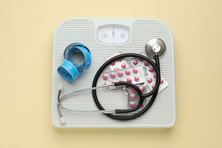 Scales with weight loss pills, measuring tape, and stethoscope on beige background, top viewの写真素材