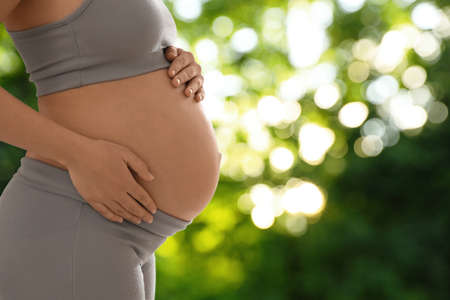 Young pregnant woman touching her belly outdoors, closeup. Space for text