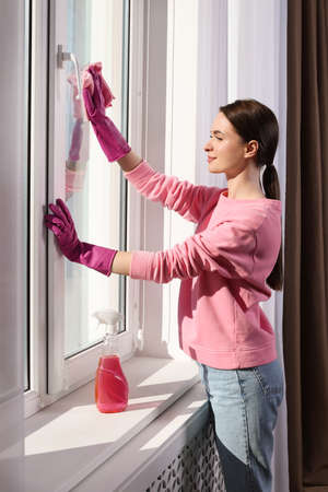 Young woman cleaning window glass with rag at homeの写真素材