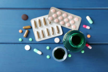 Bottle of cough syrup, measuring cup and pills on blue wooden background, flat layの写真素材