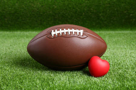 american football ball and heart on green grassの写真素材