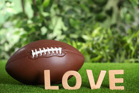 American football ball and word Love on green grass against blurred background. Space for textの写真素材