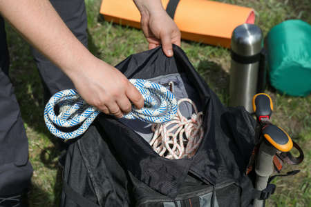 Hiker putting climbing rope into backpack outdoors, closeup. mountain tourism