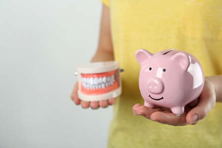 Woman holding educational dental typodont model and piggy bank on light background, closeup. Expensive treatmentの写真素材